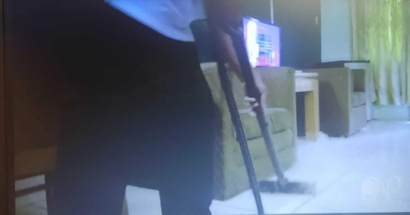 Eine Person saugt einen Teppich in einem Zimmer mit einem Fernseher und einem kleinen Tisch.