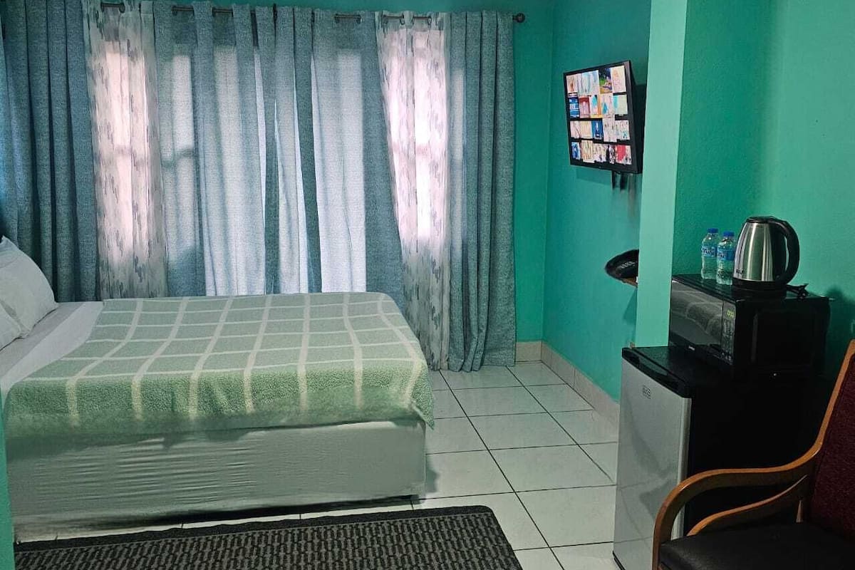 Una habitación con una cama, un escritorio con hervidor y un tablón de anuncios en la pared.