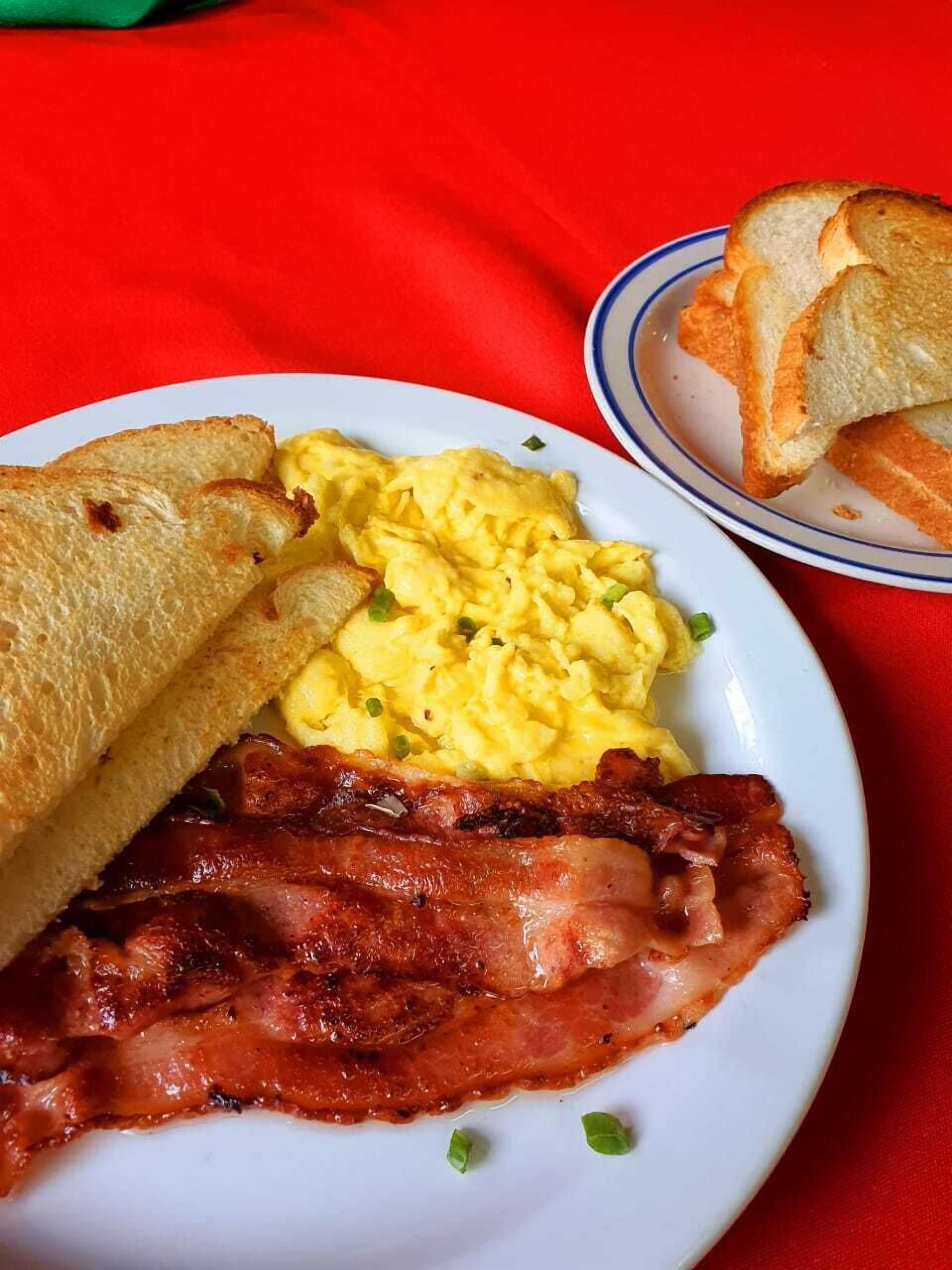 Un piatto con uova strapazzate, pane tostato e pancetta.