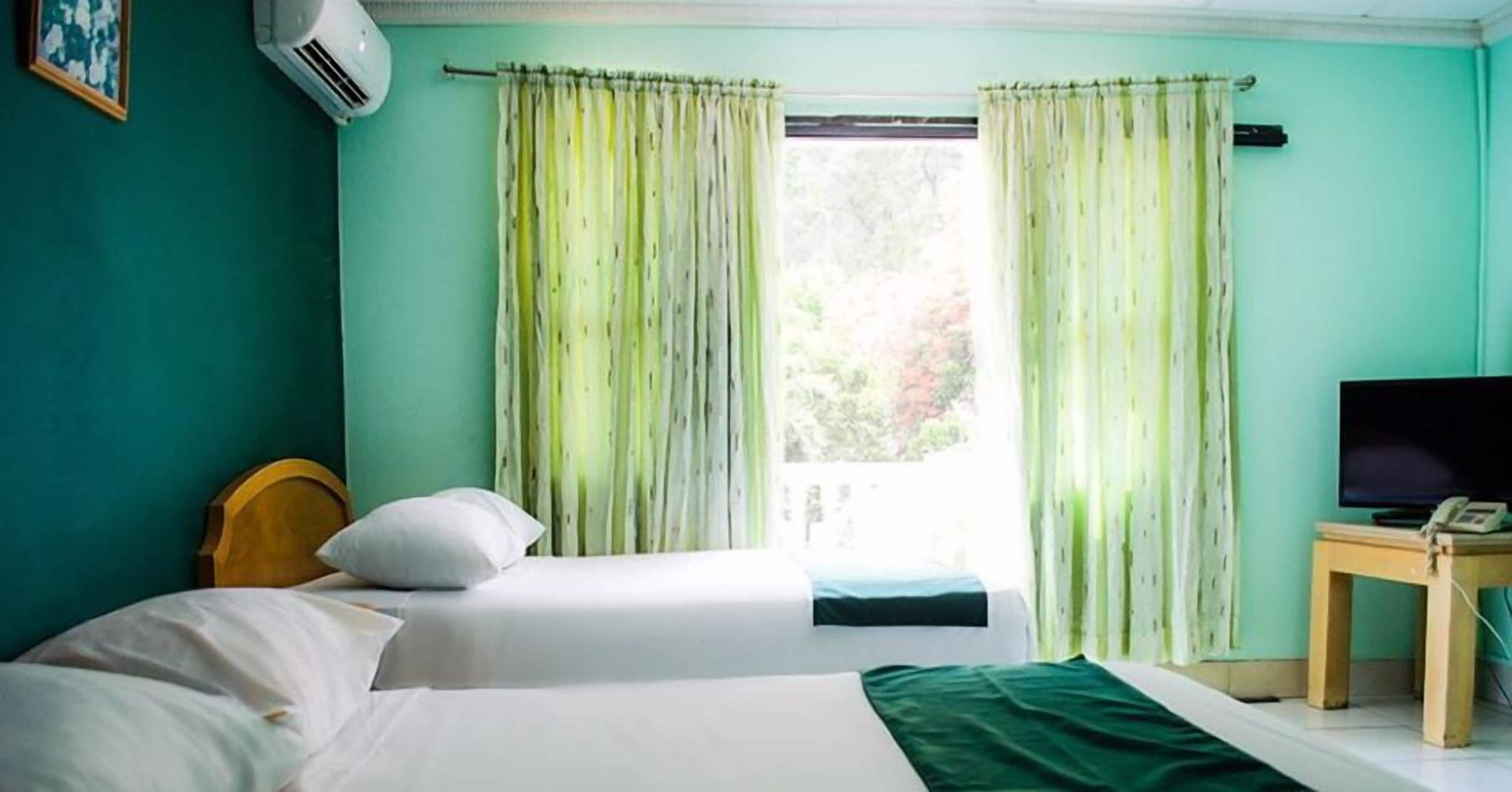 A room with two beds, a television, and a window with curtains.