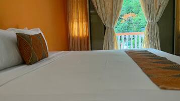 A hotel room with a large bed, white bedding, a patterned throw, and curtains.
