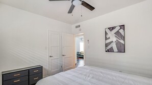 Un dormitorio con cama, cómoda, ventilador de techo y puerta que da a otra habitación.