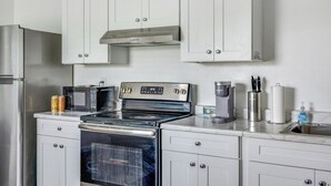Cocina compacta con armarios blancos, refrigerador de acero inoxidable, microondas, estufa y cafetera.