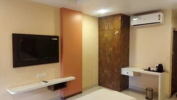 A room with a TV mounted on the wall, a wardrobe, a desk with a chair, and a bed.