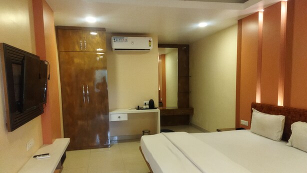 A hotel room with a bed, a desk, a mirror, an air conditioning unit, and a television. - Assam Lodge (Guwahati)