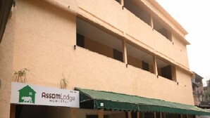 A building with a sign for Assam Lodge, featuring a green awning and multiple windows. - Assam Lodge (Guwahati)