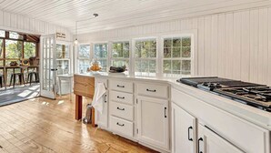 Une cuisine avec des meubles blancs, une cuisinière et de grandes fenêtres.