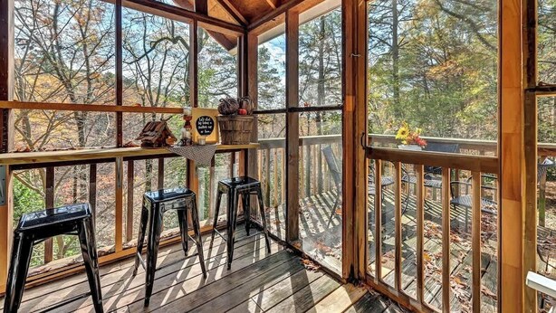 Une terrasse en bois avec une rambarde en bois, deux tabourets de bar noirs et une petite table sur laquelle est posé un panneau.