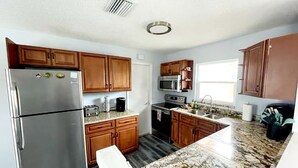 A kitchen with wooden cabinets, a stainless steel refrigerator, a microwave, and a granite countertop. - Sarasota Home Away From Home (Sarasota)