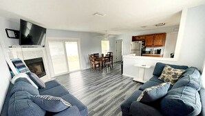A modern living room with two sofas, a TV mounted on the wall, a dining area with chairs, and a kitchen with cabinets. - Sarasota Home Away From Home (Sarasota)