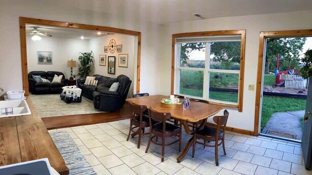 Uma sala de estar com uma mesa de jantar de madeira, dois sofás de couro preto, uma mesa de centro e uma janela grande com vista para o exterior.