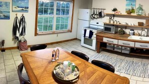 Uma cozinha com mesa de madeira, cadeiras, geladeira, micro-ondas e janela com vista para o verde.