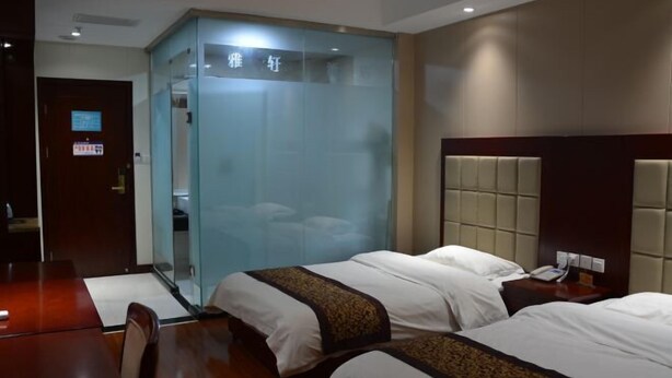 A hotel room with two beds, a wooden desk, a glass partition, and a dark-colored door.