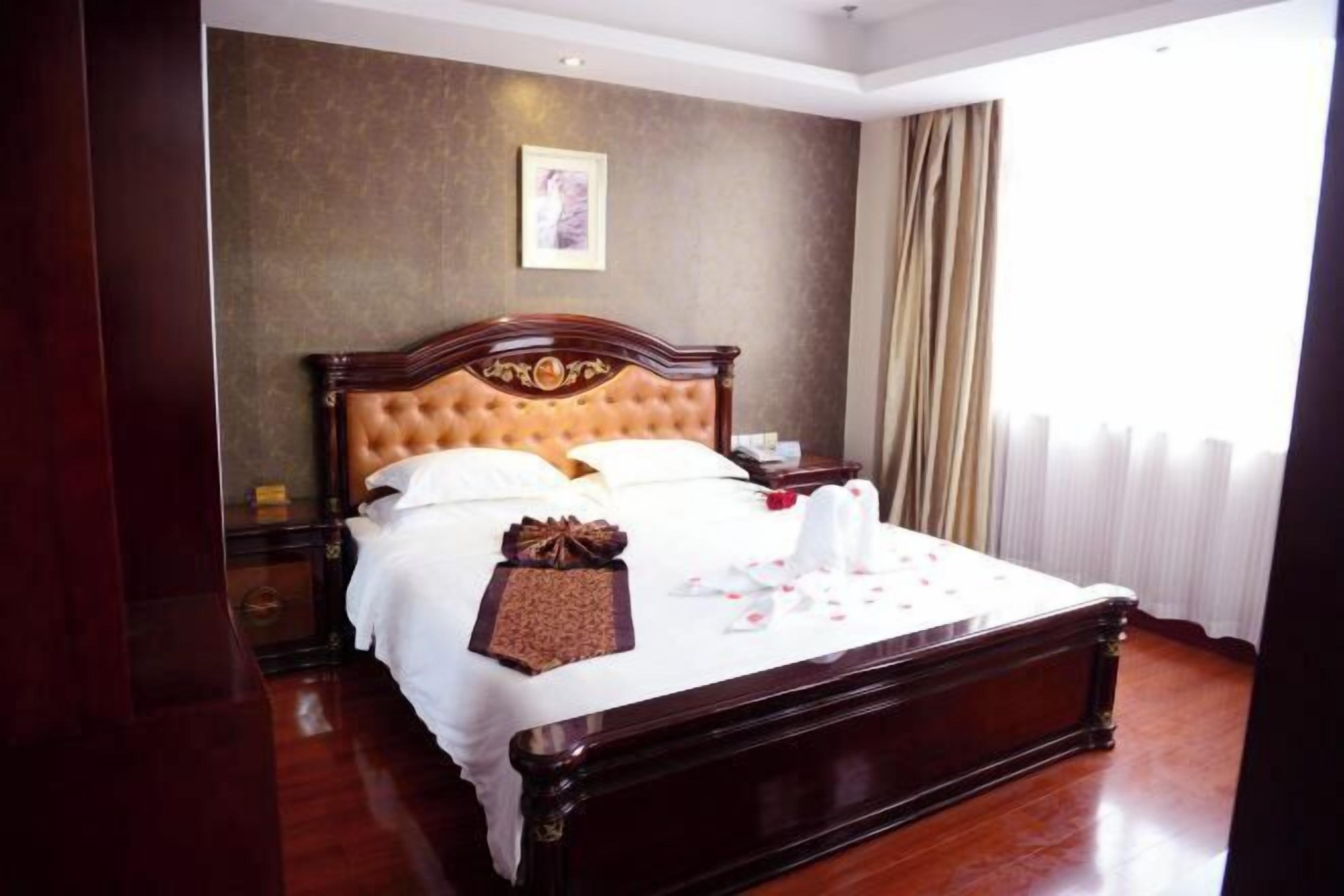 A large, ornate bed with a wooden frame and tufted headboard, a bedside table, and a framed picture on the wall.