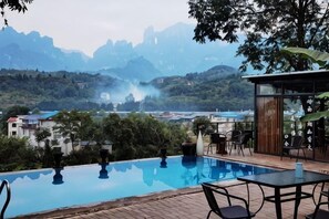 Una piscina con vista sulle montagne, un tavolo con sedie e un piccolo edificio con parete in vetro.