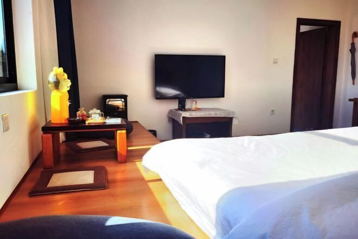 A hotel room with a bed, a desk with a lamp, a TV, and a window.
