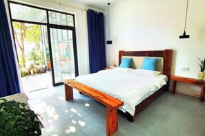 A bedroom with a large bed, a bench, a nightstand, and a view through a glass door. - Tianshe Hostel (Zhangjiajie)