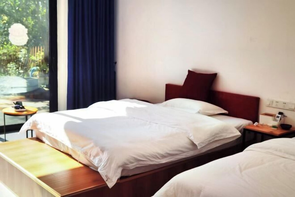 A hotel room with two beds, a small bedside table, a nightstand, and a window with curtains.