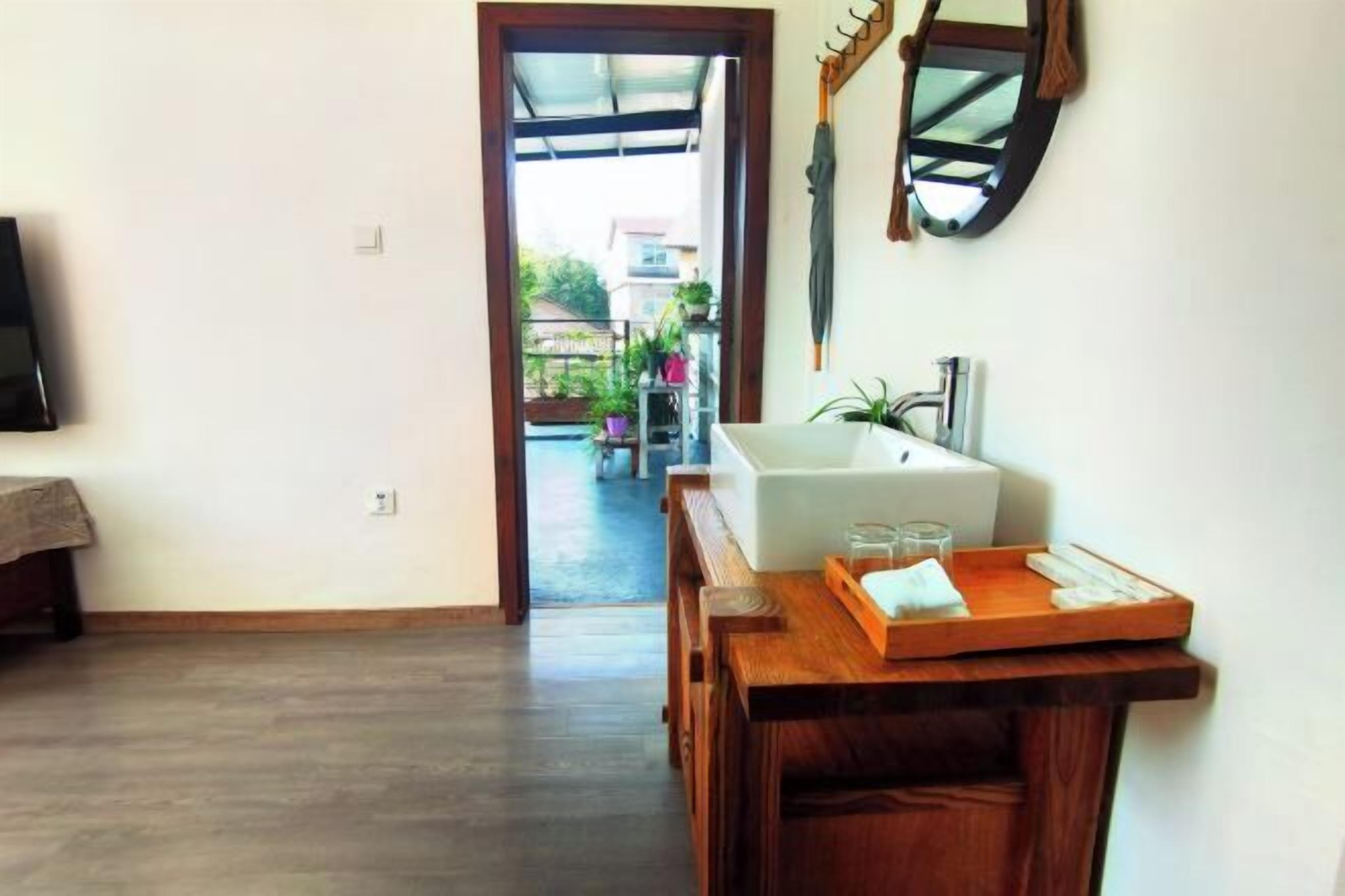 Een kamer met een houten vloer, een wit bad, een houten tafeltje met een dienblad en uitzicht op een balkon met planten.
