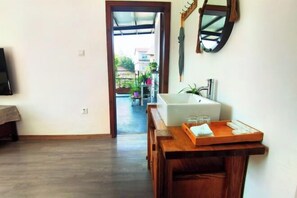 A room with a wooden floor, a white bathtub, a wooden table with a tray, and a view of a balcony with plants. - Tianshe Hostel (Zhangjiajie)