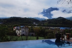 A pool with a view of mountains and a village in the background. - Tianshe Hostel (Zhangjiajie)