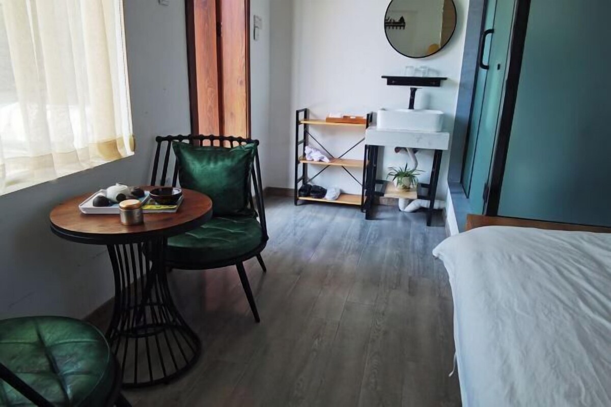 A hotel room with a bed, a dining table with chairs, a small kitchenette, and a window with curtains.