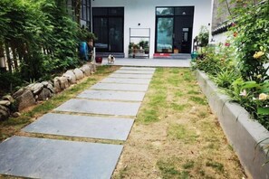 A pathway leading to a modern building with a glass door, surrounded by a garden with a stone border and various plants. - Tianshe Hostel (Zhangjiajie)