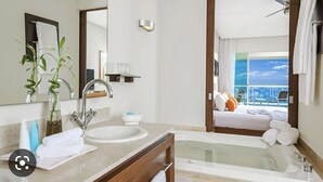 Ein modernes Badezimmer mit einer großen Badewanne, einem Doppelwaschbecken und einem Spiegel. Auf der Ablagefläche liegen Handtücher und Toilettenartikel.