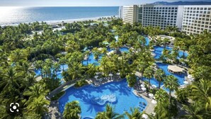 Ein Resort mit mehreren Schwimmbecken, umgeben von Palmen, einem Strand und einem großen Hotelgebäude.