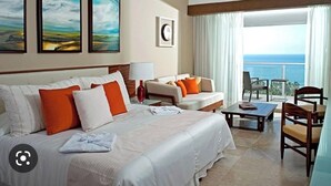 Ein Hotelzimmer mit einem großen Bett, zwei Sofas, einem Esstisch und Meerblick.