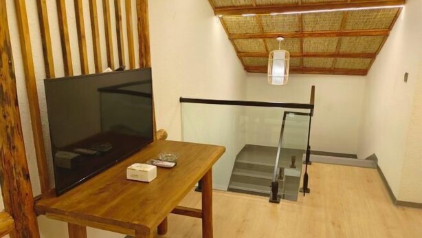A room with a wooden table, a flat-screen TV, and a staircase with a glass railing. - Southern Sichuan Bamboo Sea Qingyuan Homestay (Changning)