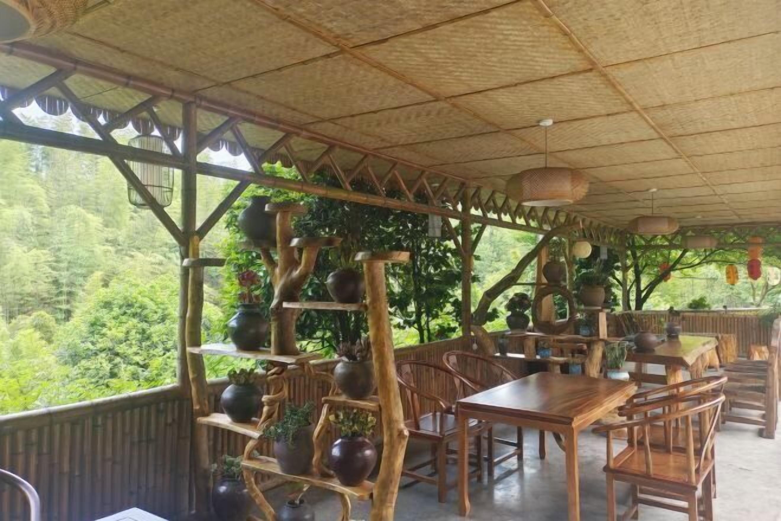 Un área de comedor al aire libre con mesas y sillas de madera, rodeada por una celosía de bambú y plantas en macetas.