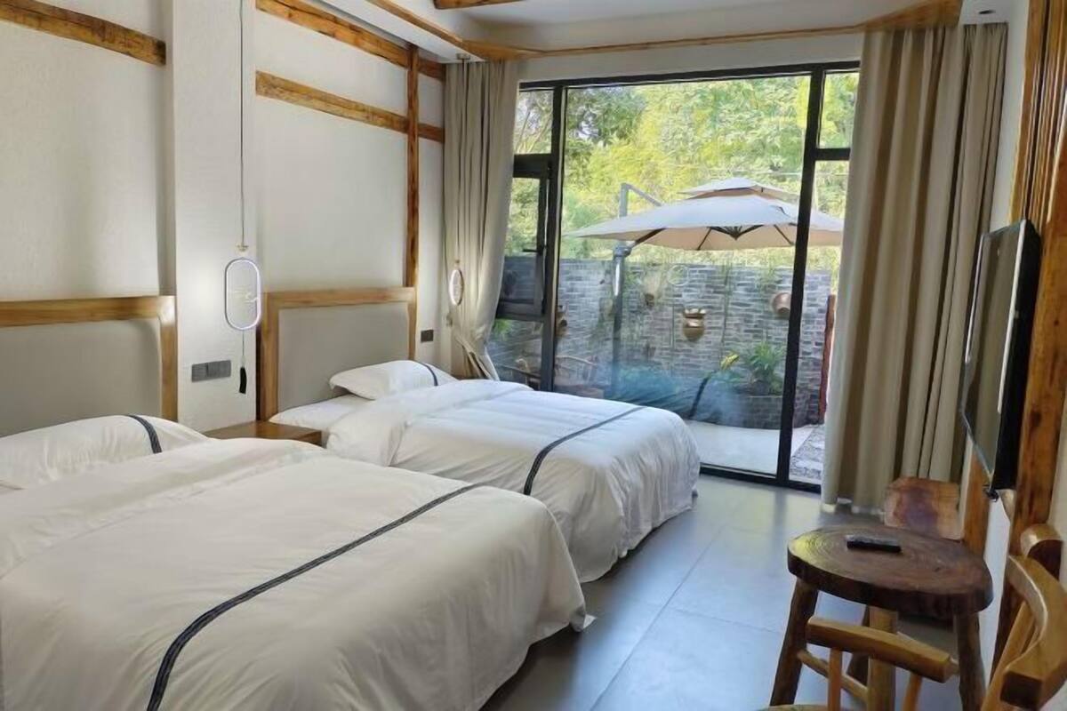A hotel room with two beds, a wooden chair, a TV, and a large window with an umbrella.