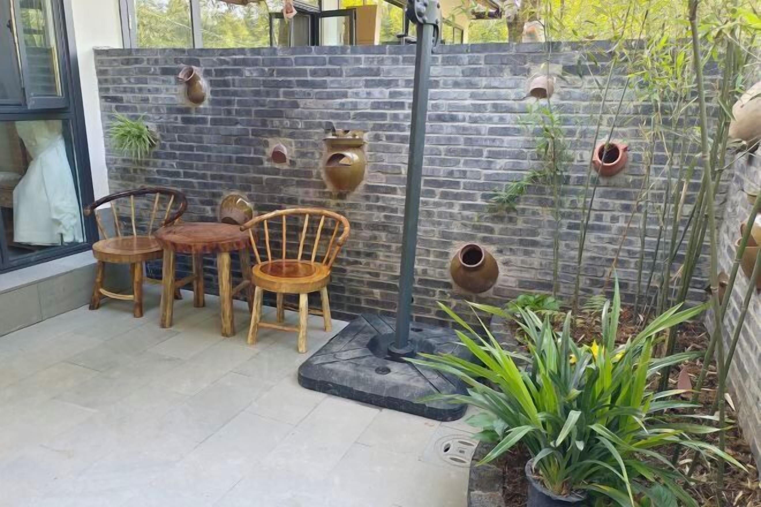 Un patio con pared de ladrillo, dos sillas de madera, una mesa y plantas en macetas.