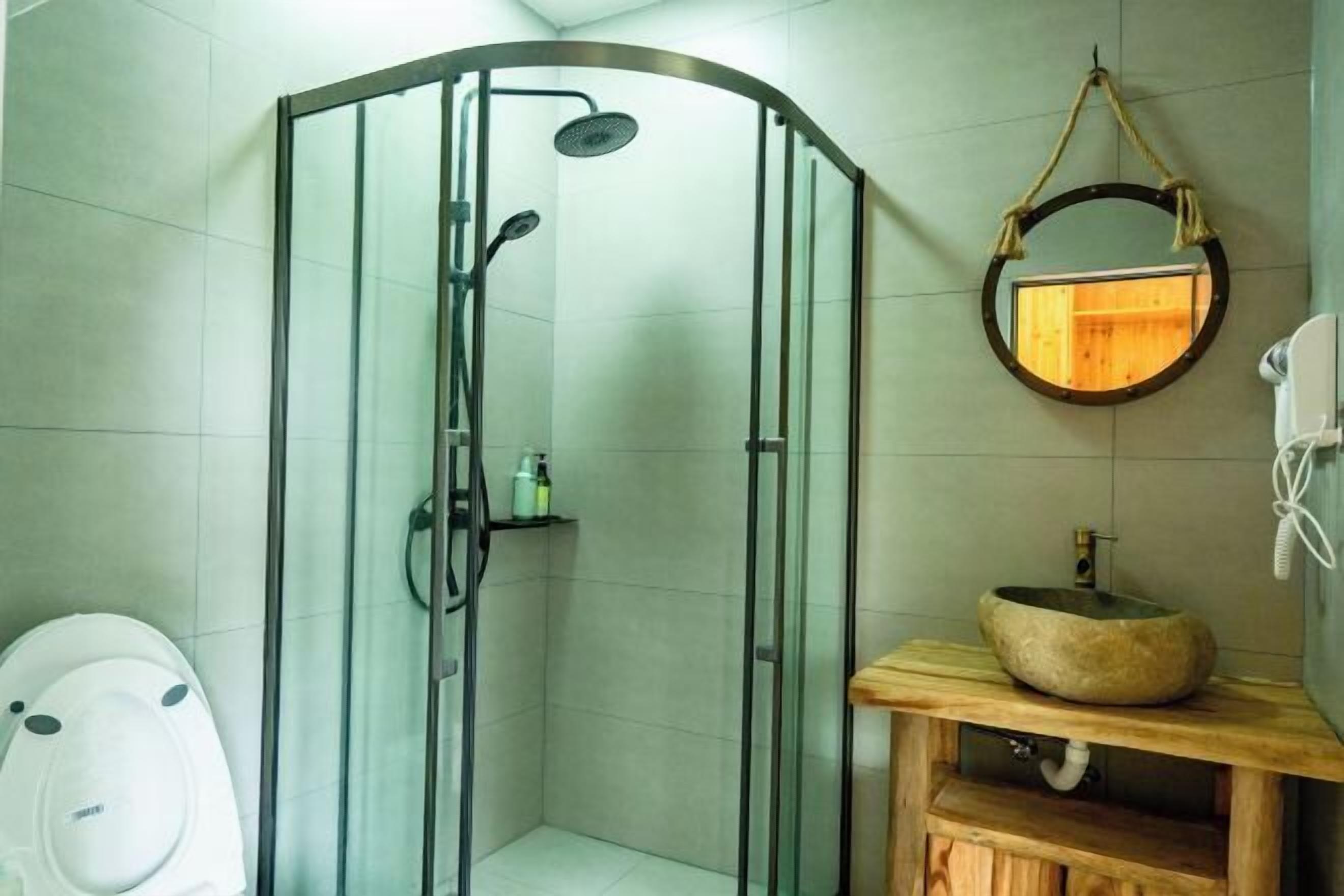 Un baño con ducha envuelta en vidrio, un espejo redondo, tocador de madera y un inodoro.