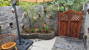Un mur de briques orné de jardinières suspendues, une porte en bois, un banc et un petit espace jardin.