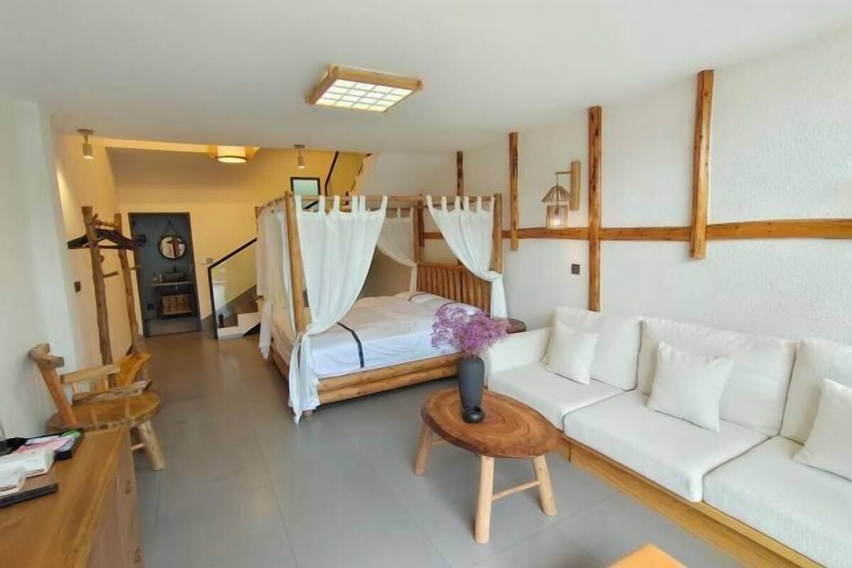 A room with a bed, a white sofa, a wooden coffee table, and a staircase in the background.
