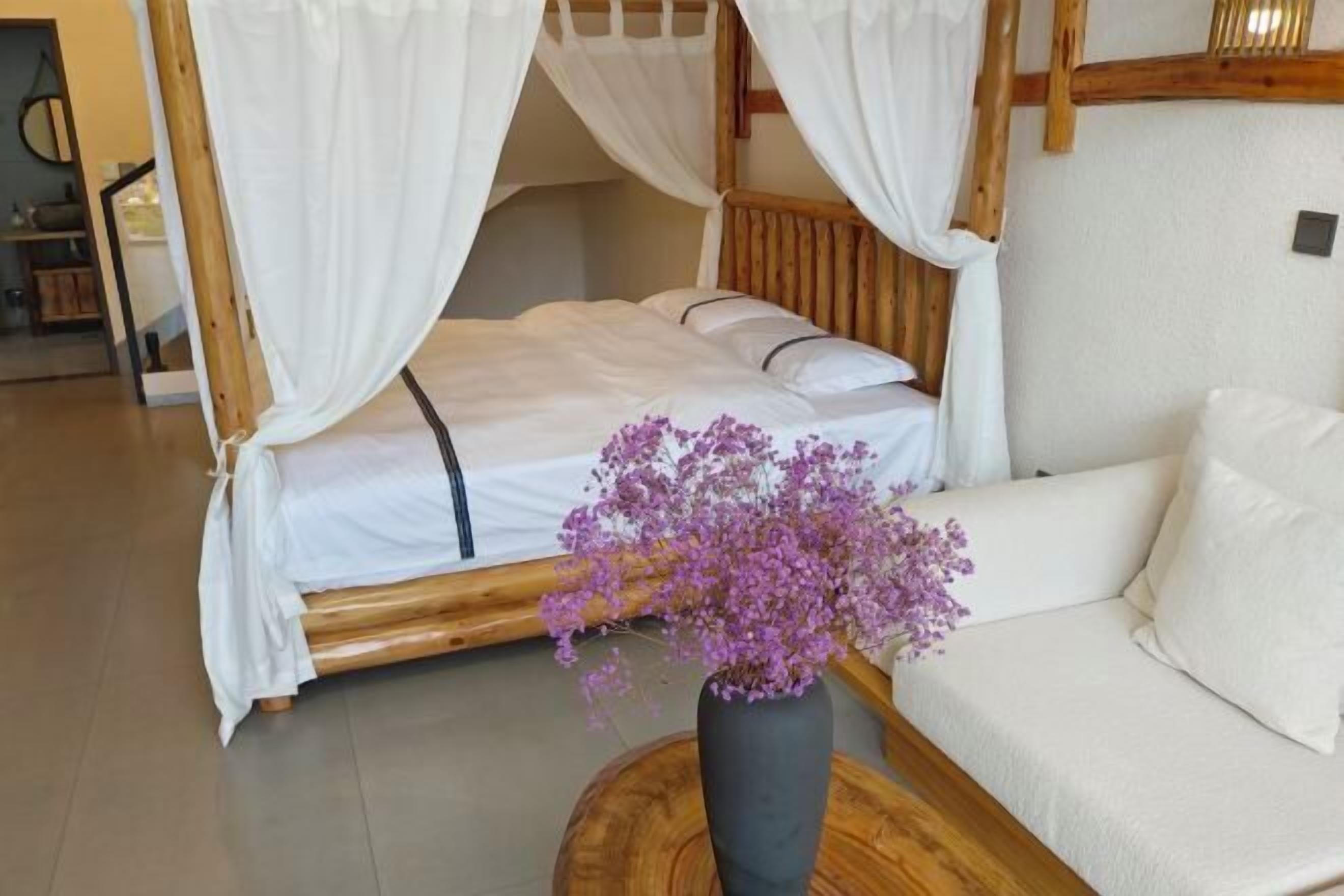 A bed with a canopy, a vase with purple flowers, and a sofa.