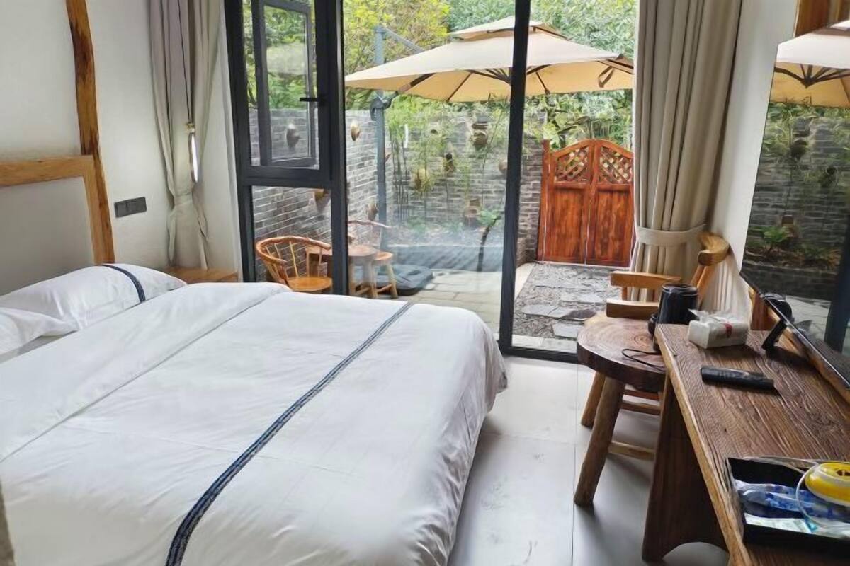A hotel room with a bed, a desk, a chair, and a large window with an umbrella.