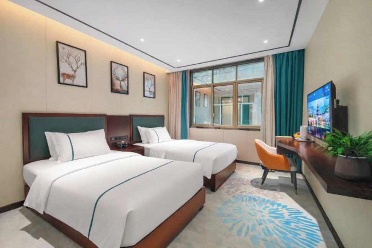 A hotel room with two beds, a desk with a chair, a television, and artwork on the wall.