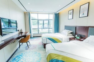 A hotel room with two beds, a desk, a chair, a TV, and a large window.