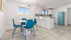 Una cocina moderna con armarios blancos, un refrigerador azul y un comedor con sillas azules y una mesa blanca.