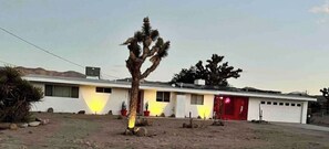 Un edificio a un piano con tetto piatto, un'anta di garage rossa e un piccolo albero in primo piano.