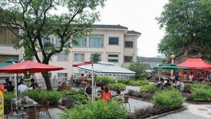 Un área de café al aire libre con mesas y sillas, rodeada de follaje y protegida por sombrillas.