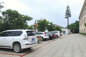 Un estacionamiento con varios coches aparcados en filas, un edificio de techo plano y árboles al fondo.
