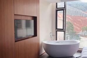 A modern bathroom with a freestanding bathtub, a mounted TV, and a large window with a view of a construction site.