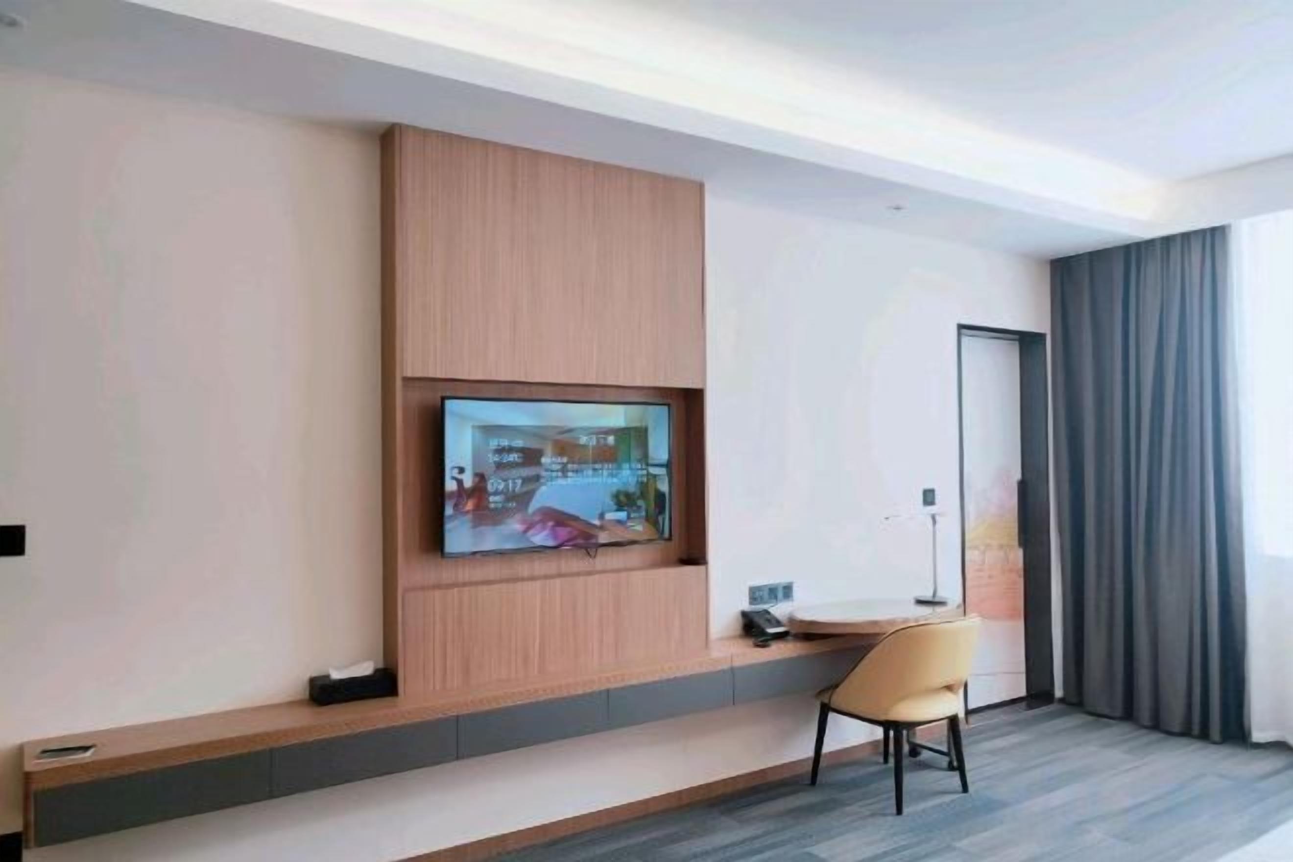 Ein modernes Hotelzimmer mit einem wandmontierten Flachbildfernseher, einem kleinen Tisch mit einem Stuhl und einer mit Vorhängen versehenen Tür.