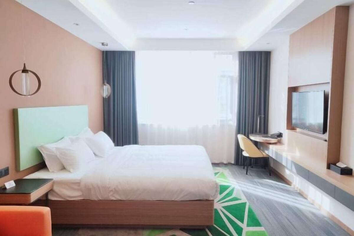 Habitación de hotel con cama, escritorio, silla, televisor y ventana con cortinas.