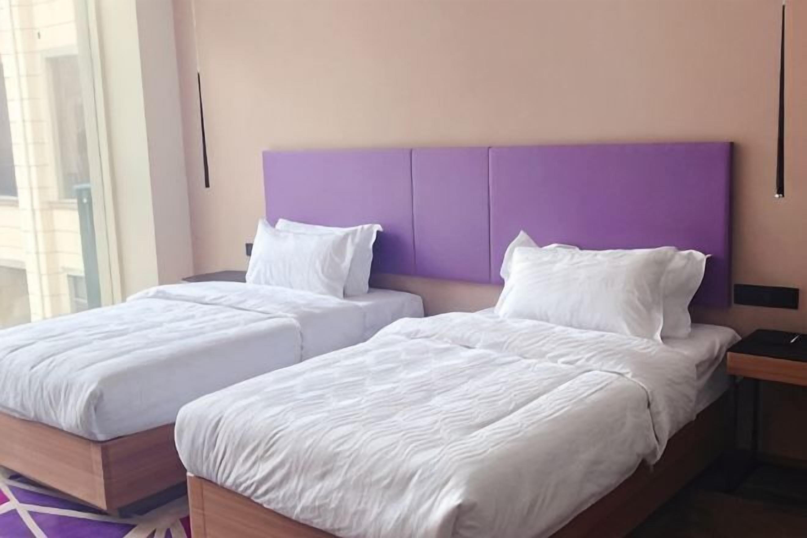 Habitación de hotel con dos camas, un cabecero morado y una mesita de noche.