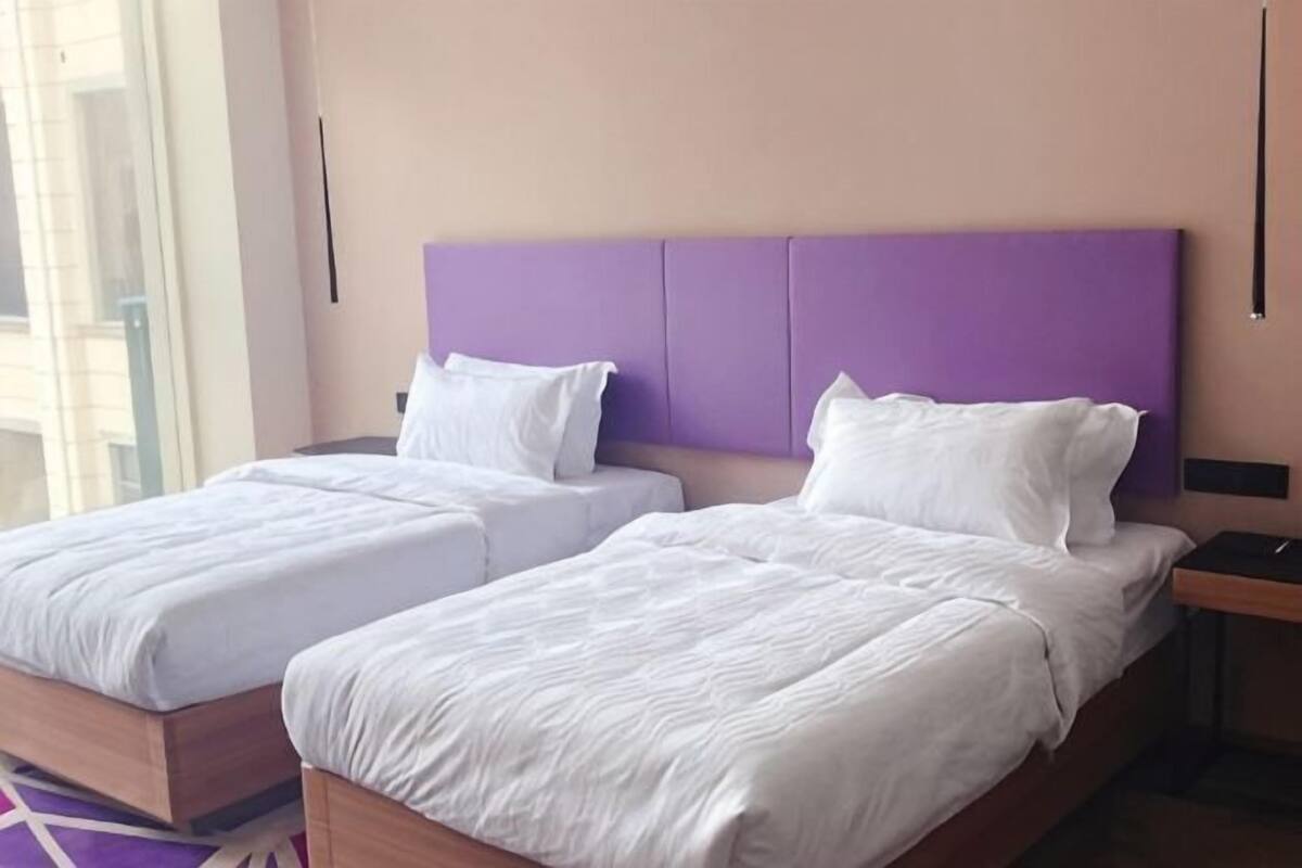 Habitación de hotel con dos camas, un cabecero morado y una mesita de noche.